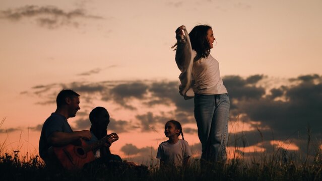 Family picnic with children, singing, dancing to guitar in nature. Happy family camping outdoors summer vacation. Parents children enjoy outdoors, playing guitar, singing, dancing together at sunset.