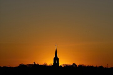 Obraz premium Sunset backdrop with a spire and cross silhouette on the horizon
