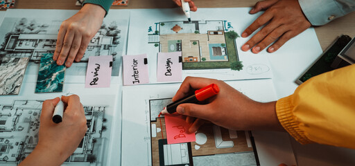 A dynamic team collaborates on an interior design project, showcasing hands taking notes, colorful markers, and detailed plans spread across a table, highlighting creative teamwork. SACTR