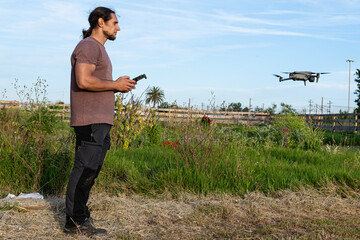 Farmer piloting drone over cultivated field using remote controller