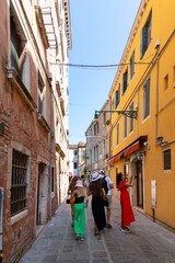 Tourists exploring colorful narrow street in Venice. Group of tourists walking and taking photos along a vibrant, narrow alleyway between historic buildings in Venice, Italy.