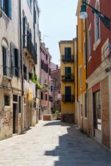 Colorful narrow street with laundry in Venice. A charming Venetian alley with colorful facades, shuttered windows, balconies, and laundry drying in the sunlight, capturing authentic Italian life.