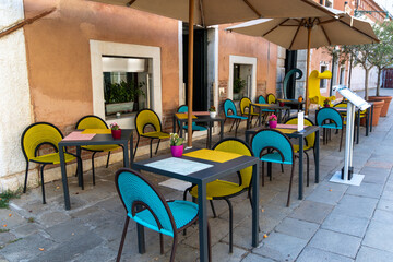 Colorful outdoor cafe seating on Venetian street. Brightly colored chairs and umbrellas decorate a modern outdoor cafe terrace along a quiet pedestrian street in Venice, Italy.