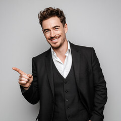 Professional full body image of confident businessman in elegant black suit with white shirt, pointing finger gesture with smile, modern executive studio portrait
