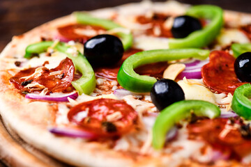 Pizza with chorizo ​​sausage, mozzarella cheese, green pepper and black olives. Rustic wooden background. Soft focus.	