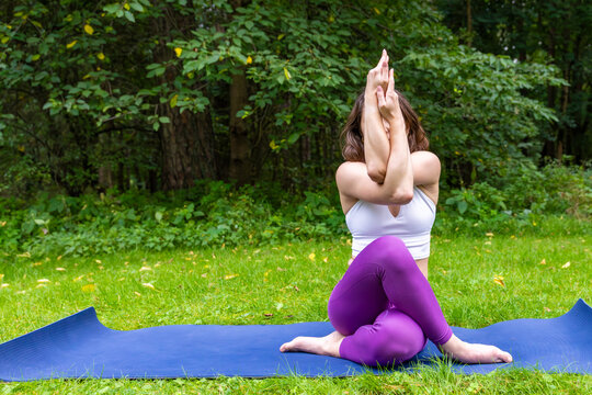 Woman in seated eagle pose with arms crossed on yoga mat in park. Balance and concentration in outdoor yoga.