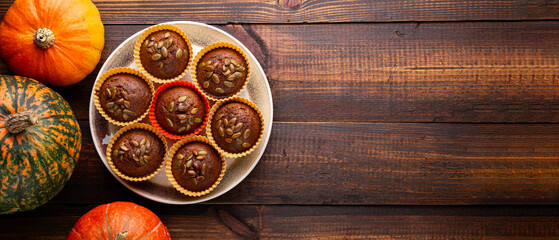Autumn pumpkin cupcakes or baked muffins with fresh pumpkin and pumpkin seeds for Thanksgiving day on dark wooden background. Web banner, copy space for text