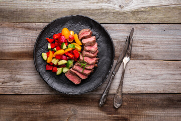 beef steak with fresh vegetable salad on black plate, top view, copy space