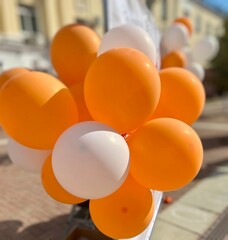 Bright orange and white balloons clustered together outdoors, showcasing a festive and vibrant atmosphere. Captured with a soft focus background to highlight the colors.
