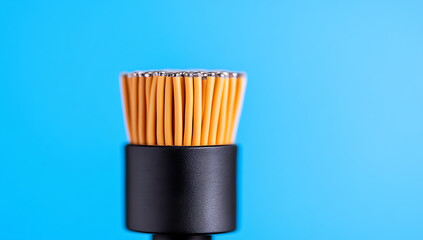 Close-up of a black cylindrical base holding up an arrangement of orange filaments against a vibrant blue background. Minimalist studio shot.