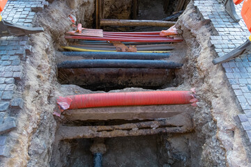 Various electrical wires are buried beneath a street walkway. Cobblestones are removed to allow underground cable installation