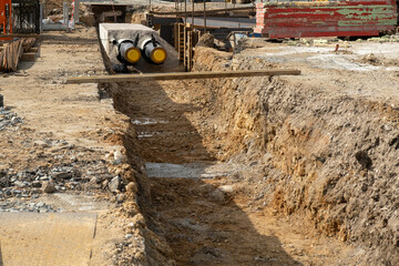 open trench at a construction site reveals two large black tubes with yellow caps that are ready to be buried. The surrounding ground