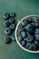 Fresh blueberries in a clear glass bowl on a green surface filled with more berries