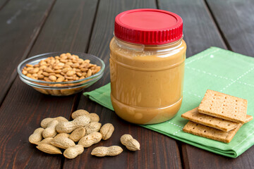 Jar of Creamy Peanut Butter with Peanuts and Snack Crackers on Table