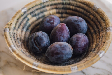 six purple italian plums in small, handwoven basket
