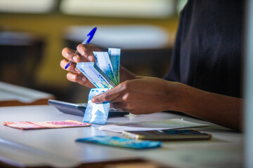 Dark skinned African person working on desk holding counting Ghanaian cedi notes in hand. accounting concept