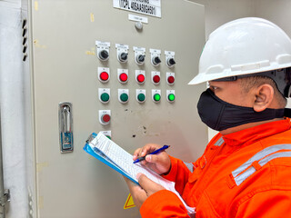 Industrial worker inspecting control panel with switches and indicators checking readings on clipboard ensuring safety protocols following procedures maintaining operational integrity