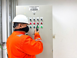 Industrial worker wearing safety gear using a walkie-talkie and inspecting a control panel with buttons and switches in a plant for safety and efficiency maintenance process