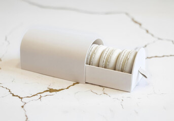 White drawer packaging with a handle and white macarons on a marble countertop.