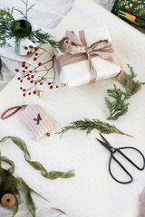 Merry Christmas and Happy Holidays! Stylish christmas present with green branch, ribbons, ornaments, scissors and festive paper on rustic table flat lay. Wrapping holidays gifts