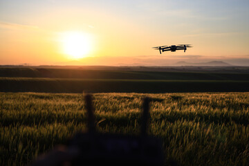 Drone monitoring a field during morning light in spring A drone monitors a wheat field during the morning light, controlled via a controller in the foreground photo