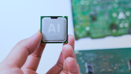 Hand holding AI-labeled microchips with blurred circuit boards in background, representing artificial intelligence hardware.