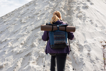 Back view of hiker woman climbing sandy hill with backpack