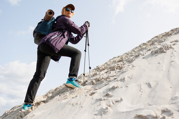 Sporty female hiker climbing sandy slope with poles