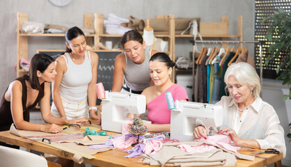 Busy women of different ages sewing and drawing with teacher at dressmaking class