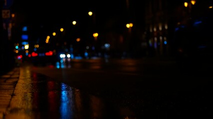 Wet asphalt reflecting city lights at night with passing cars. City lights reflecting on wet asphalt at night, with passing cars creating streaks of light and color