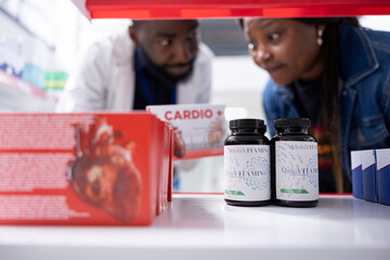Black medical expert showing cardiology care medicine on pharmacy shelves, discussing treatment and heart health options with a pharmacist who provides detailed medication advice for self care.