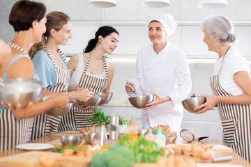 Young lady chef of restaurant during open culinary master class tells and shows girls visitors stages of cooking spicy cream sauce for meat, pasta