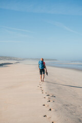 Lonely barefoot backpacker man walking by sandy Portugese beach in morning on the Atlantic ocean...