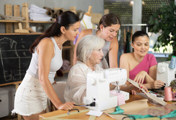 Elderly woman teacher shows group women how to sew on sewing machine in class