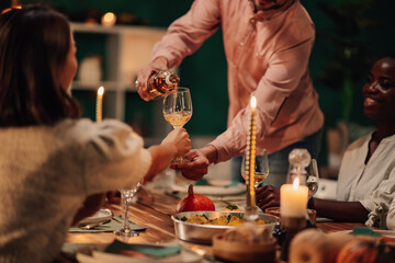 Man pouring white wine into woman's glass during thanksgiving dinner
