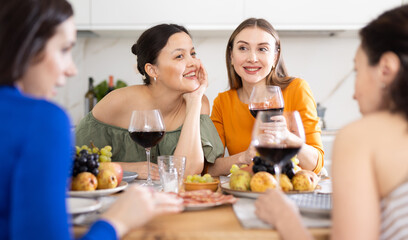Casual evening where group of cheerful carefree besties sharing wine, dining together, and chatting in cozy home kitchen ..