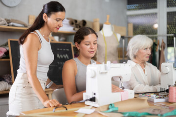 Positive young woman sewing with stitching-machine controlled by teacher during dressmaking classes