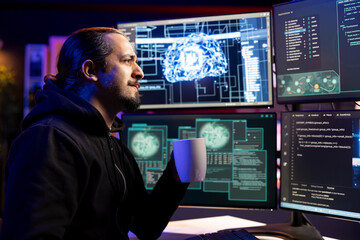 Smiling cybercriminal holding coffee mug coding on PC, trying to evade security with stealth malware. Evil man drinking beverage uses script hiding malicious code from detection systems