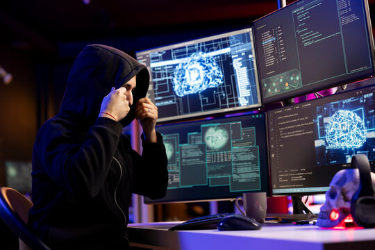 Hooded hacker in underground HQ doing ransomware attacks using AI to hold company systems hostage and demand money. Evil man using neural networks tech to hack enterprise networks, encrypting files