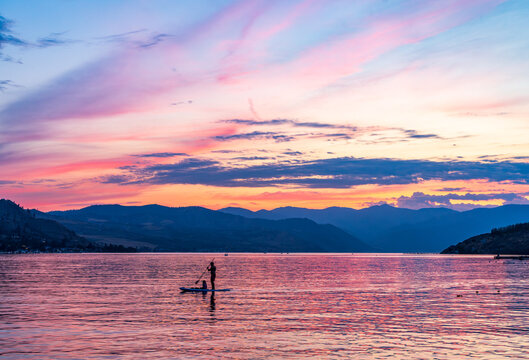 Dramatic sunset over Lake Chelan with silhouette of couple paddling on board and sky reflected in the smooth water of the lake in WA - Powered by Adobe