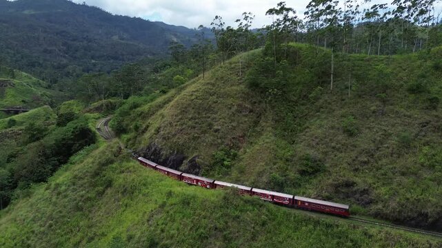 Aerial drone view of a scenic red train journey through the lush green hill country of Sri Lanka