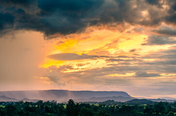 Beautiful scenery of the rainy season, evening light shining through rain clouds, rain, mountains, green rice fields and trees in the countryside of Chiang Rai Province, Thailand.