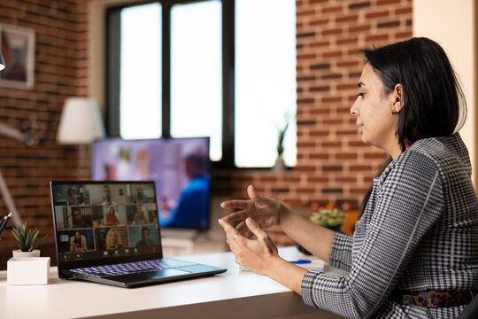 Businesswoman networking with global professionals over video call in home office. Female manager looking towards laptop, making hand gestures during remote team meeting to discuss company challenges.