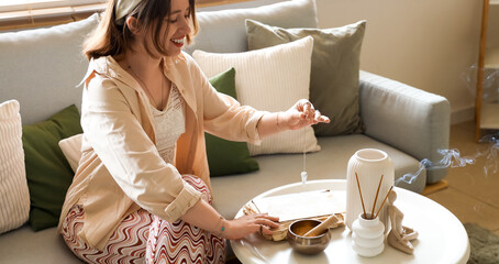 Young witch with pendulum and spell book on table at home