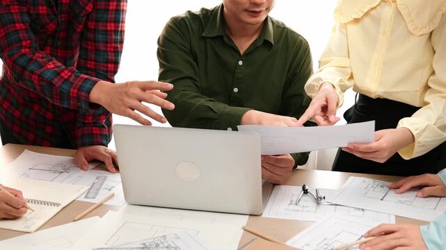 Smart architect and safety engineer discussion about building plan on table with architectural document, measurement tools and wooden block scatter around at modern office. Closeup. Delineation.