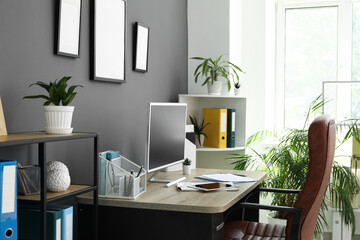 Interior of office with workplace, armchair, modern computer, houseplant and shelving unit near black wall
