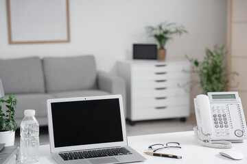 Fototapeta premium Blank laptop with water bottle and telephone on desk in office