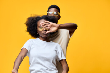 Stylish couple posing against a vibrant yellow background, showcasing modern fashion The woman is wearing a casual white t shirt, while the man has a light colored top and sunglasses