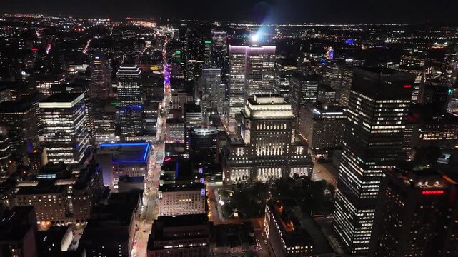 Drone pulls back over a downtown Montreal street at night, surrounded by skyscrapers, revealing the CIBC Tower and Sheraton hotel