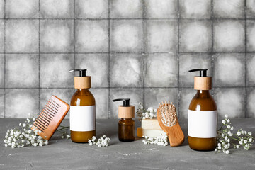 Composition with bottles of shampoo and flowers on table near grey grunge tile wall